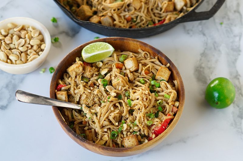 Bowl of vegan peanut butter pad Thai topped with crushed peanuts, green onions, and lime wedges